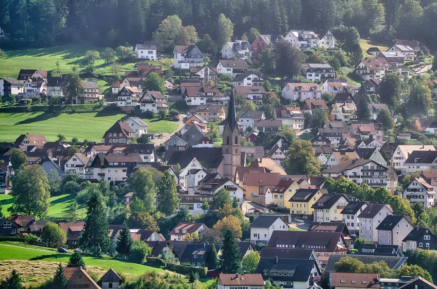 Blick über eine kleine Ortschaft mit Kirche zwischen grünen Hügeln